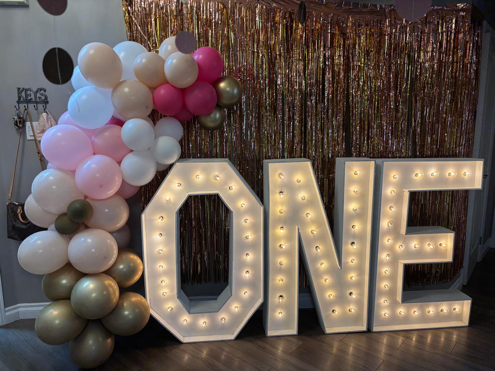 Marquee letters that spell out "ONE" framed with balloon decor