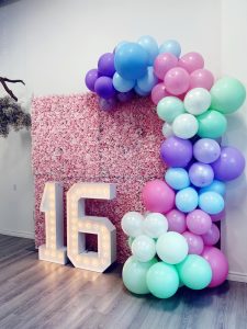 Stratford marquee number rental with a flower wall which is framed by a balloon garland
