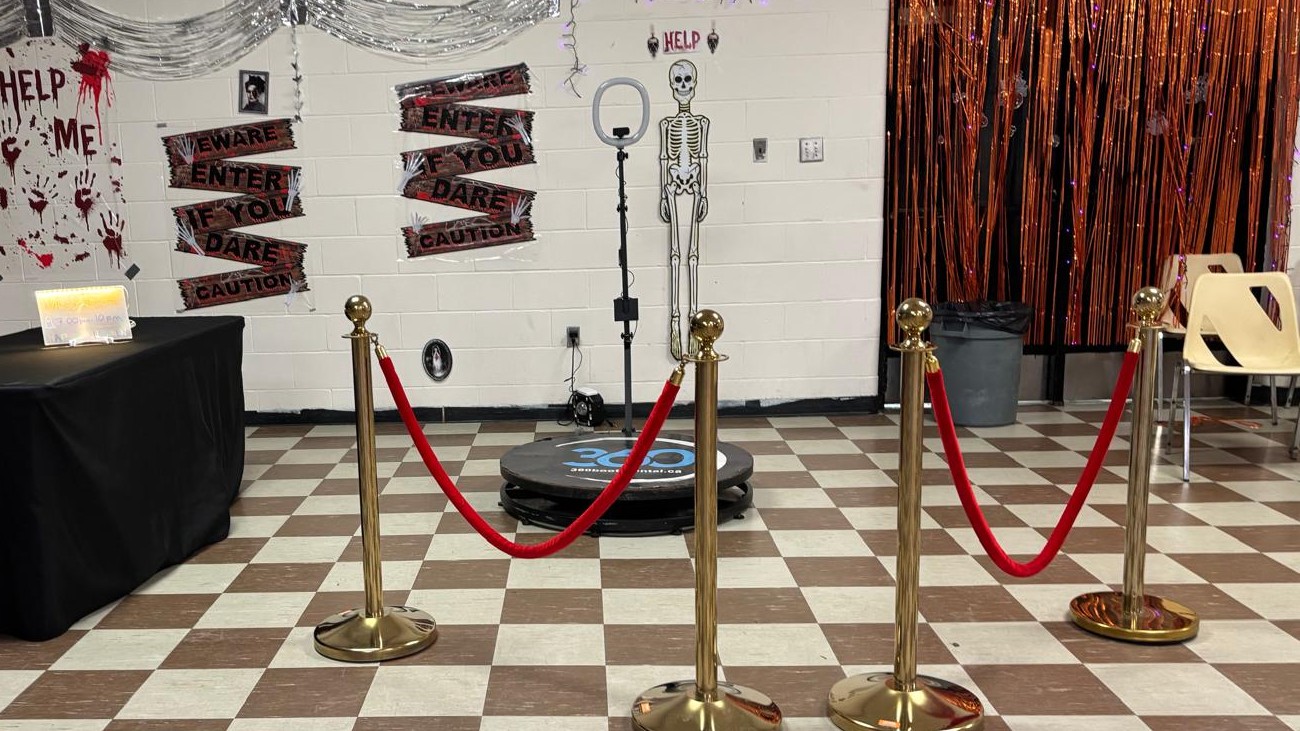 A 360 booth roped off against a decorated wall with a foil fringe curtain and a checkerboard floor